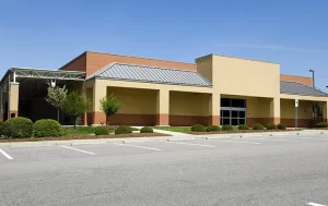 A beige and brown one-story commercial building with large windows and an empty parking lot on a clear day features Stat Pest Control signage. Small trees and shrubs line the front of the building.